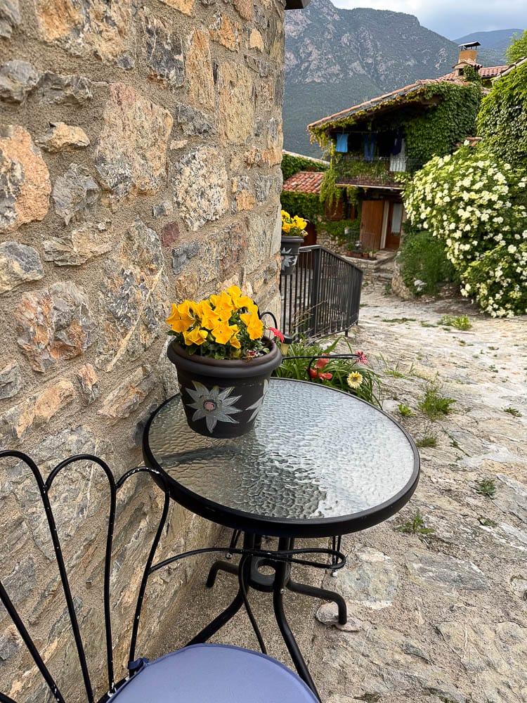 Taula amb dues cadires i un test amb flors a l'entrada de Cal Marinall