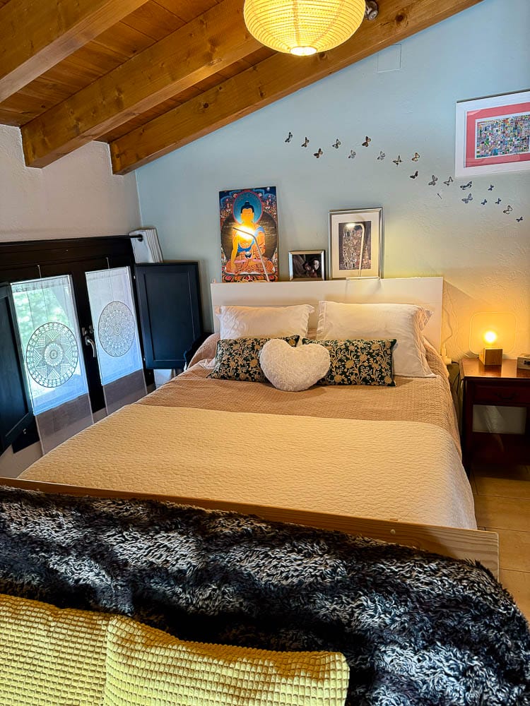 Llit doble amb coixins, una làmpada de llum càlida al sostre de bigues de fusta